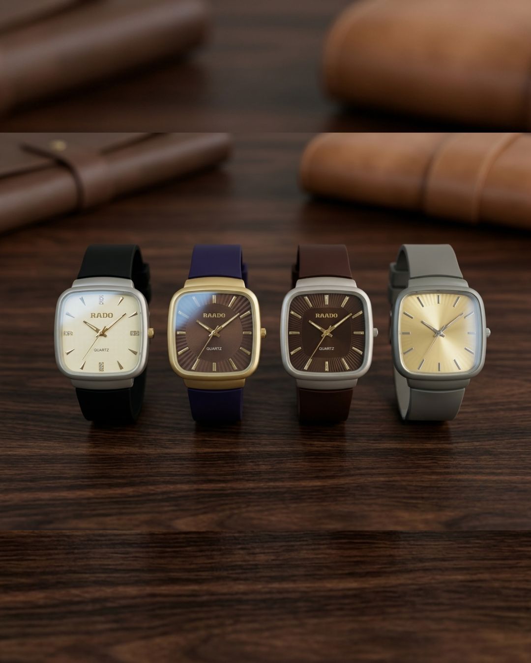 Four RAINO square analog wristwatches with square dials and different straps (black, navy blue, brown, and gray) lined up on a dark wooden table with blurred leather accessories in the background.